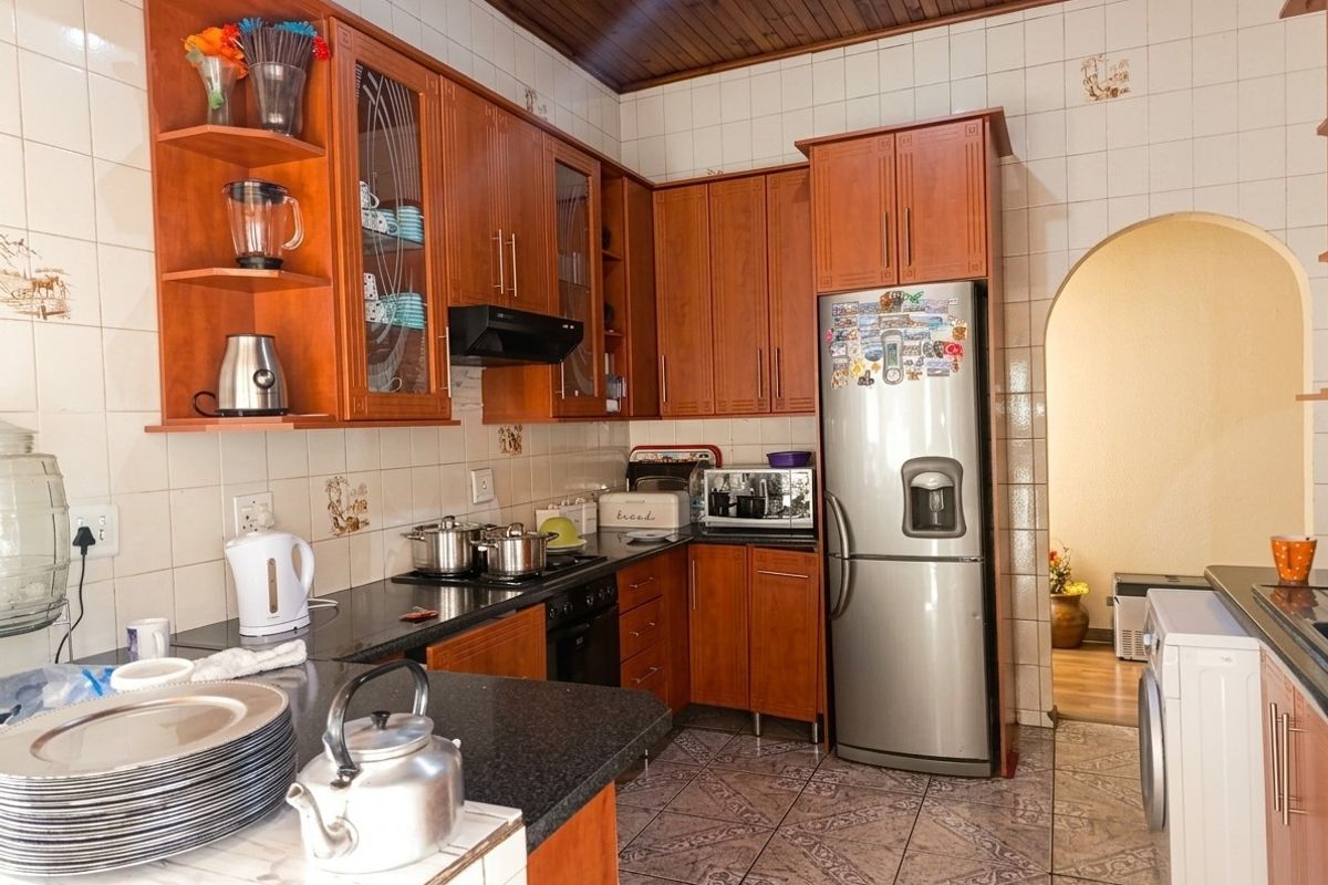 A functional kitchen featuring warm-toned wooden cabinetry, granite countertops, tiled backsplash, and a distinctive timber-paneled ceiling, leading through an archway to adjacent living areas.