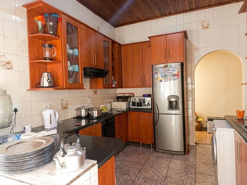 A functional kitchen featuring warm-toned wooden cabinetry, granite countertops, tiled backsplash, and a distinctive timber-paneled ceiling, leading through an archway to adjacent living areas.