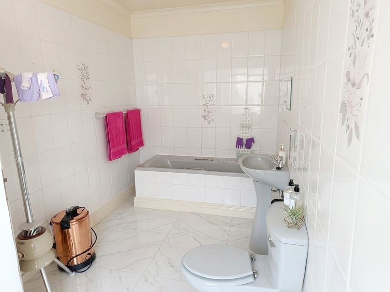 A functional bathroom featuring a built-in bathtub, pedestal basin, toilet, and white tiled walls with decorative accents.
