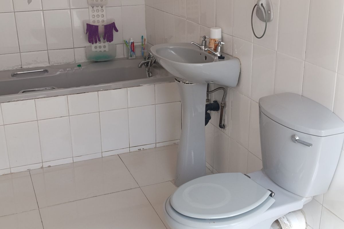 A dated bathroom featuring a grey pedestal basin, matching toilet, and bathtub with white wall and floor tiling.