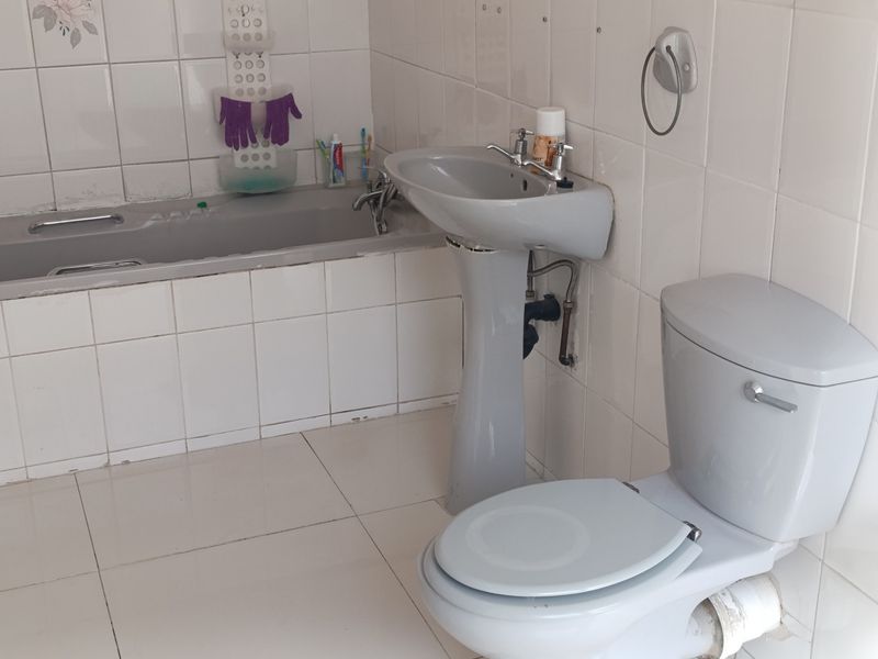 A dated bathroom featuring a grey pedestal basin, matching toilet, and bathtub with white wall and floor tiling.