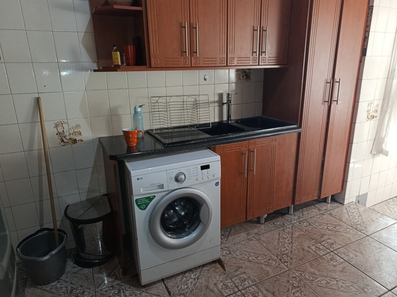 A functional laundry area featuring built-in wooden cabinetry, a double sink, and tiled finishes, providing practical utility space.
