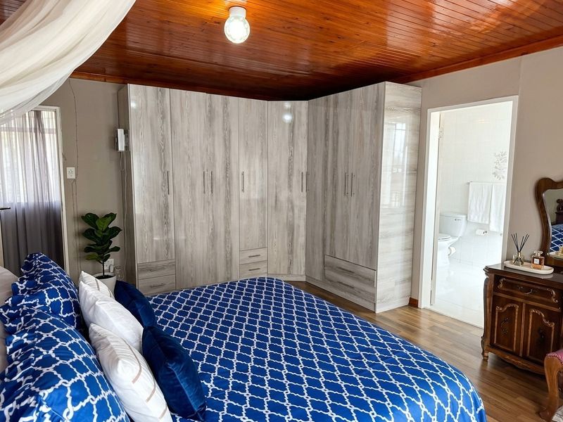 A well-maintained bedroom featuring modern built-in wardrobes, a warm timber-paneled ceiling, laminate flooring, and direct access to an en-suite bathroom.