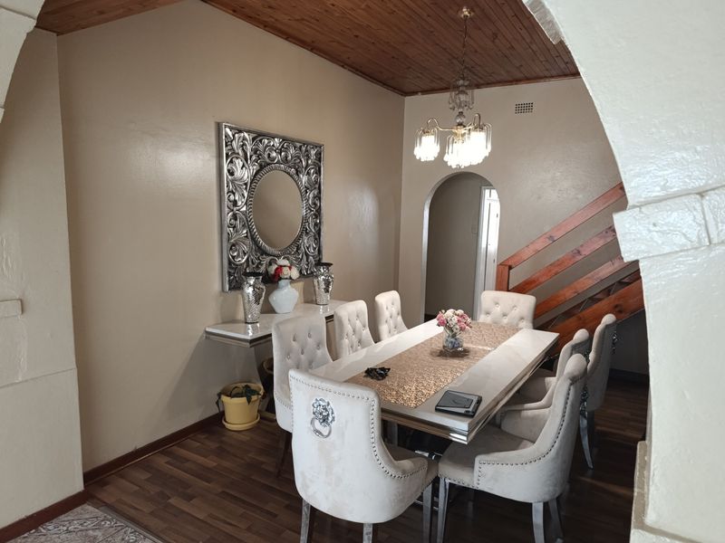 Dining room featuring a timber ceiling, laminate flooring, and a wooden staircase, framed by a decorative archway.