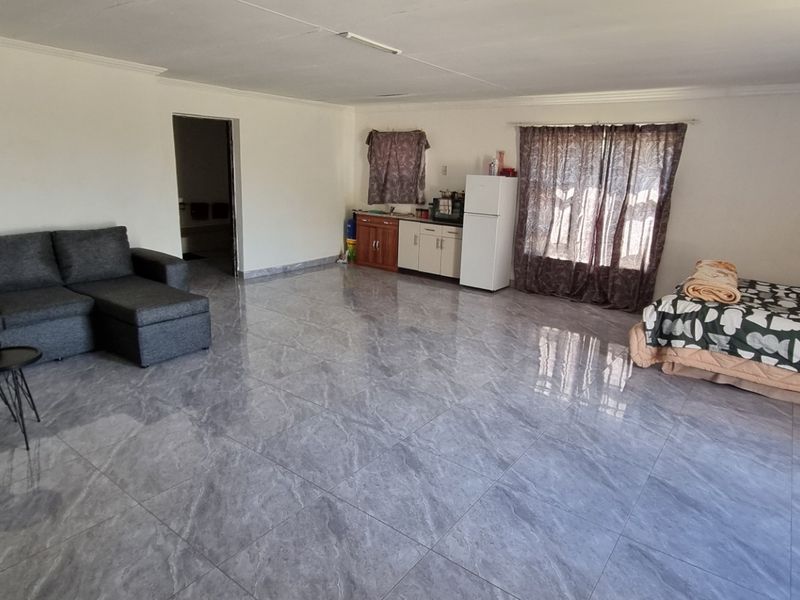 Spacious open-plan living area featuring large format grey floor tiles, a compact kitchenette, and neutral wall finishes.