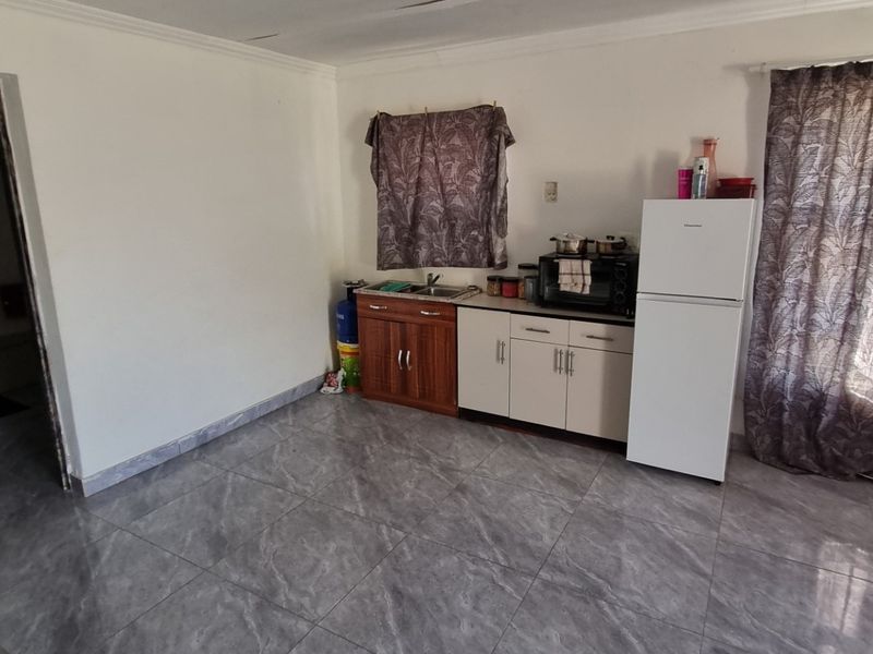 Open plan living area featuring tiled flooring and a compact kitchenette with basic cabinetry and sink.