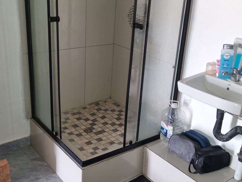 A compact bathroom featuring a shower enclosure with tiled flooring and a wall-mounted basin with exposed plumbing fixtures.