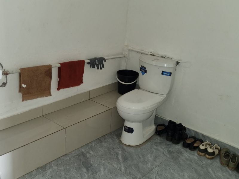 A functional bathroom featuring a wall-mounted basin, toilet, and tiled flooring, with exposed plumbing and basic finishes throughout.