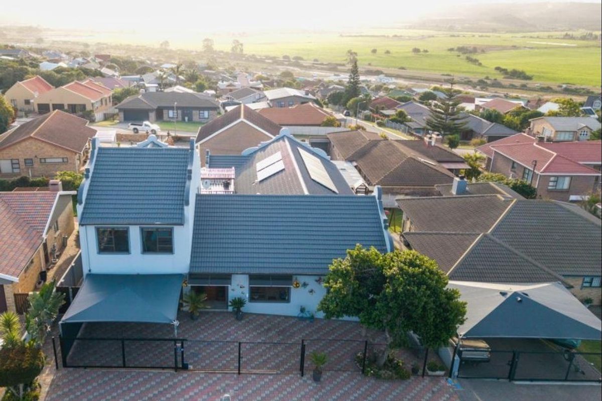 Aerial view of a residential property featuring a tiled roof with solar panels, a paved driveway, and shade sail carports in a suburban setting.