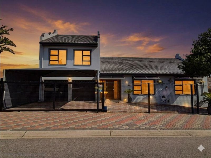 Front elevation of a two-story residential property featuring a paved driveway, carport, and secure perimeter fencing at dusk.