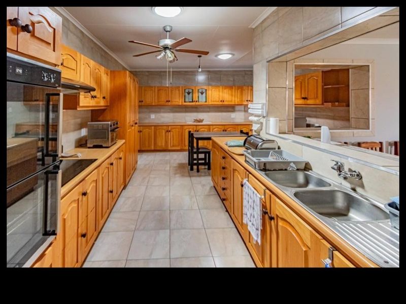 Spacious kitchen featuring extensive wooden cabinetry, double stainless steel sink, built-in oven, and a convenient pass-through window connecting to the adjacent living area.