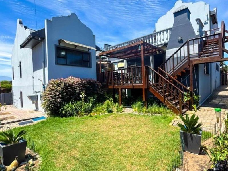 Rear view of the property featuring a raised timber deck with staircase, pergola, landscaped garden, and paved pathways.