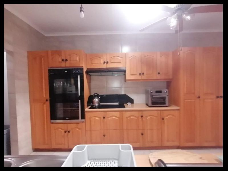 A functional kitchen featuring wooden cabinetry, a built-in oven, extractor fan, and tiled backsplash, providing ample storage and workspace.