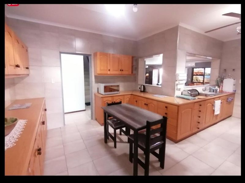 Spacious kitchen featuring extensive wooden cabinetry, tiled walls and flooring, and a convenient pass-through window connecting to the adjacent living area.