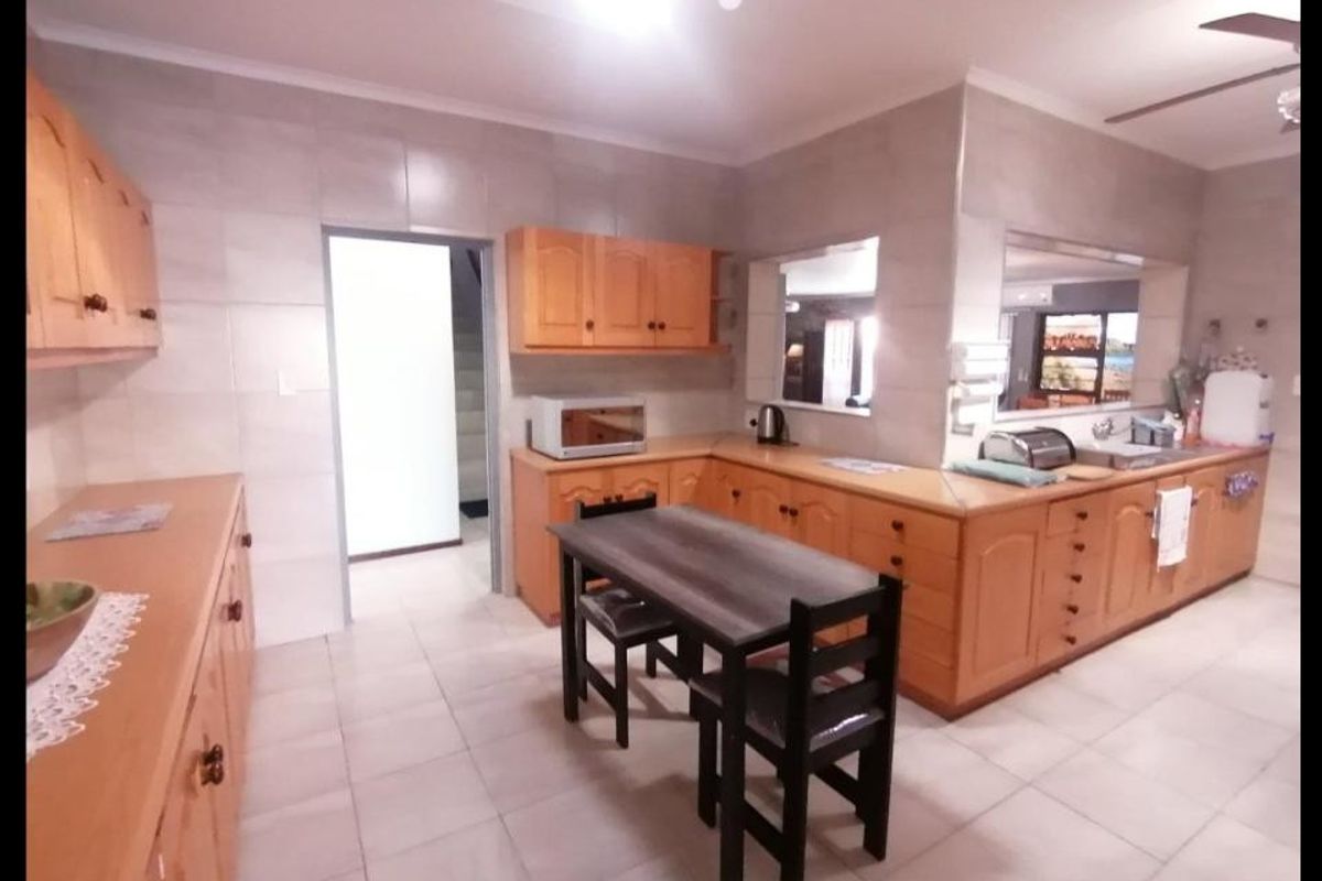 Spacious kitchen featuring extensive wooden cabinetry, tiled walls and flooring, and a convenient pass-through window connecting to the adjacent living area.