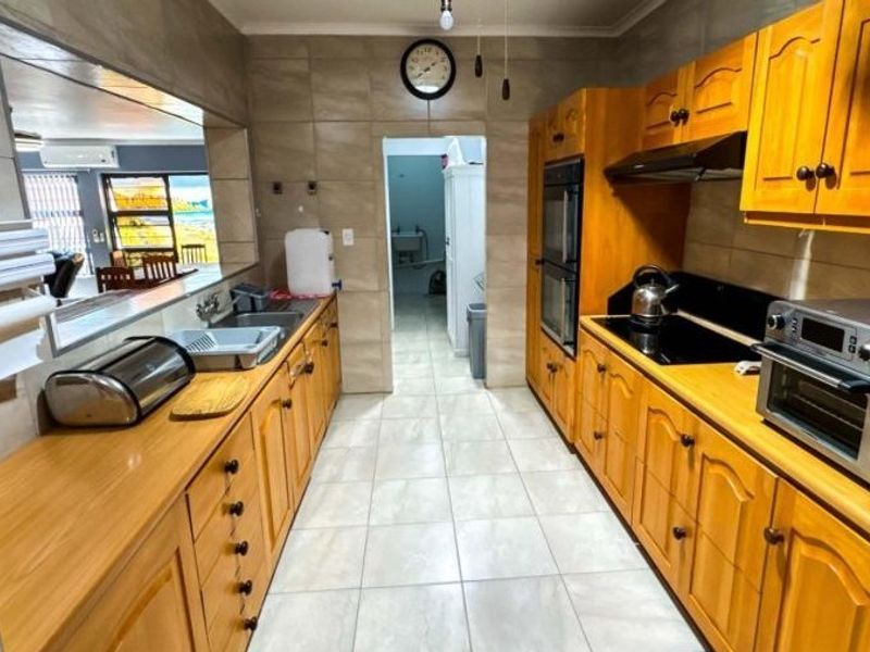 A functional kitchen featuring wooden cabinetry, built-in double oven, electric hob, and a convenient pass-through window overlooking the living area.