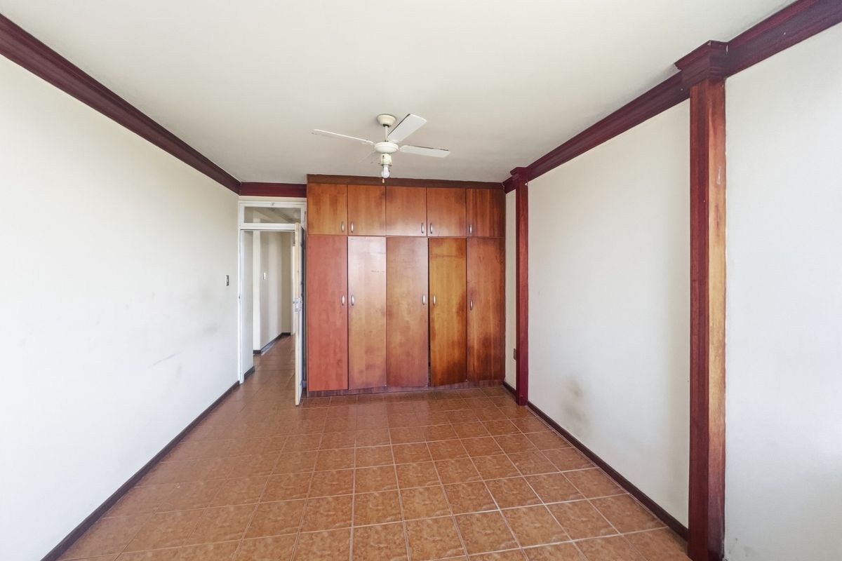 An empty bedroom featuring tiled flooring, built-in wooden cupboards, a ceiling fan, and decorative wooden trim details.