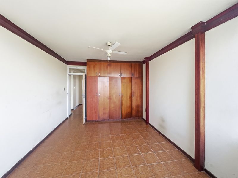 An empty bedroom featuring tiled flooring, built-in wooden cupboards, a ceiling fan, and decorative wooden trim details.