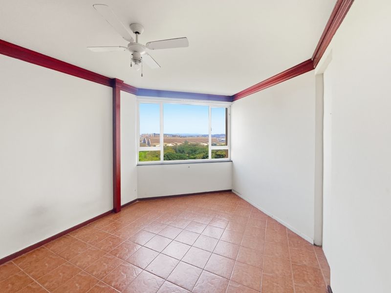 An empty living room featuring tiled flooring, a ceiling fan, and large windows offering an expansive outdoor view.