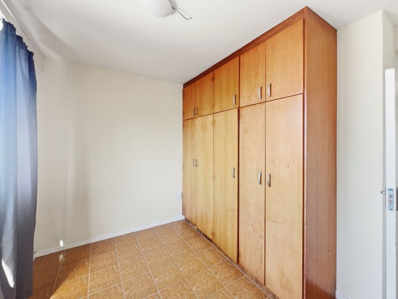 A bedroom featuring built-in wooden cupboards and tiled flooring, offering a functional space ready for personalization.