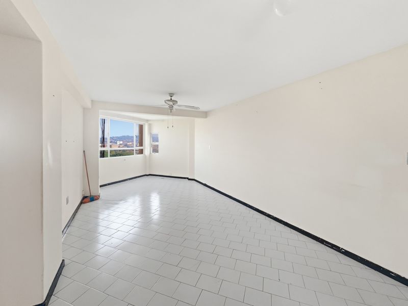 An empty, open-plan living area featuring tiled flooring, a ceiling fan, and large windows with city views.
