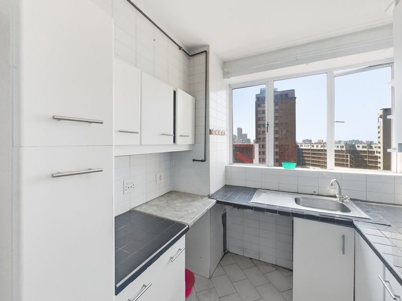 A compact, functional kitchen featuring white cabinetry, tiled countertops, and a stainless steel sink, offering a bright space with an urban city view.