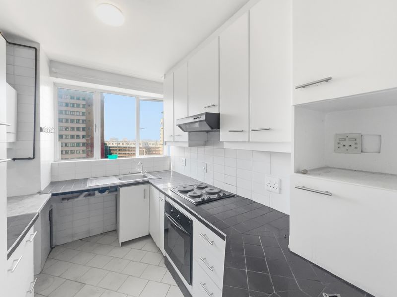 A functional kitchen featuring white cabinetry, dark tiled countertops, a built-in oven, and an electric hob, offering a clean and practical workspace.