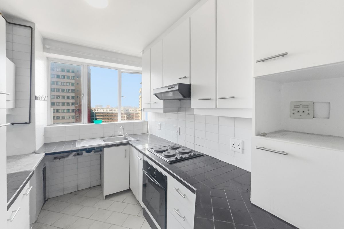 A functional kitchen featuring white cabinetry, dark tiled countertops, a built-in oven, and an electric hob, offering a clean and practical workspace.