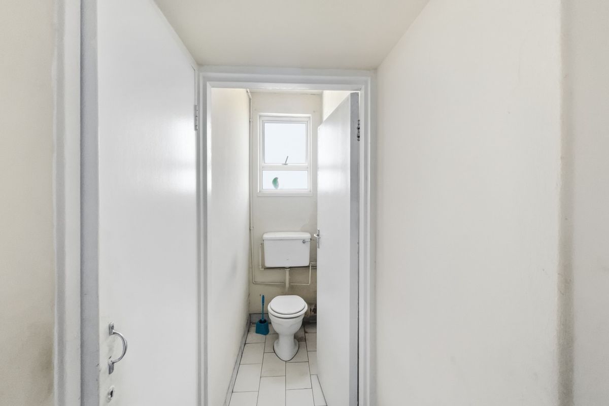 A compact, functional bathroom featuring a standard toilet, tiled flooring, and a small window, presenting an opportunity for modernization and cosmetic updates.