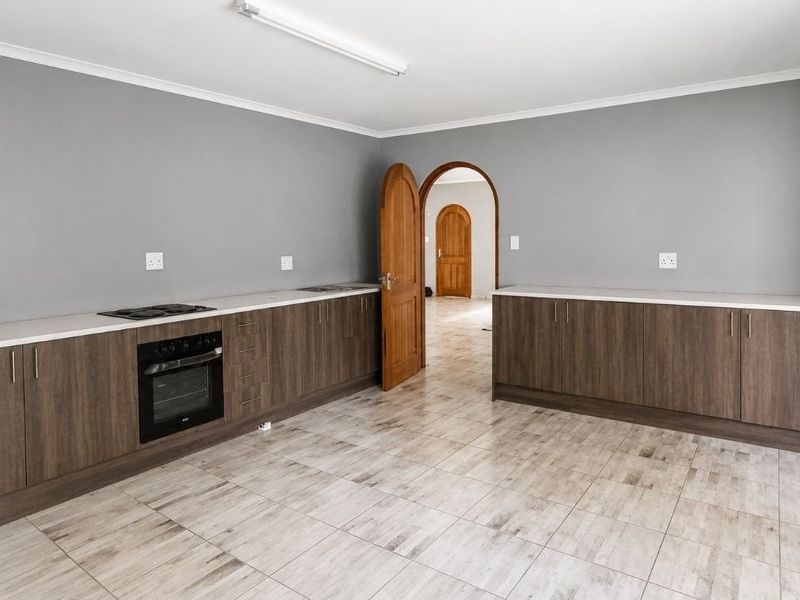 A clean, empty kitchen featuring modern wood-finish cabinetry, light countertops, integrated oven and hob, and neutral tiled flooring with an arched doorway.
