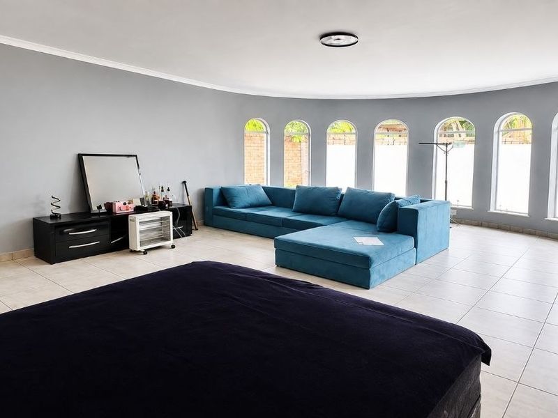 Spacious living area featuring a curved wall with multiple arched windows, neutral grey walls, and light-colored tiled flooring.
