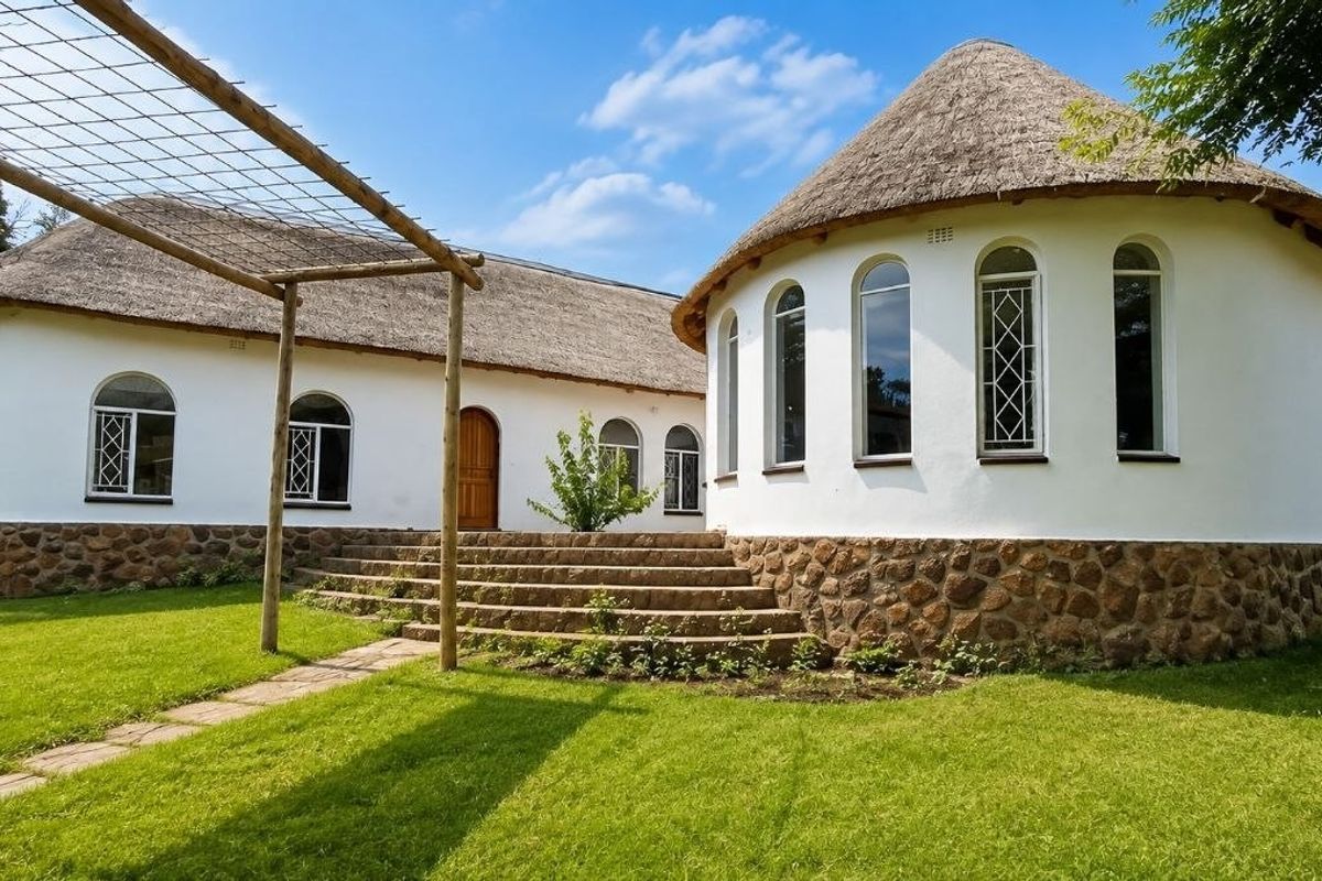 A well-maintained rear exterior view featuring a unique thatched roof design, stone cladding, arched windows, and a timber pergola leading to stone steps.