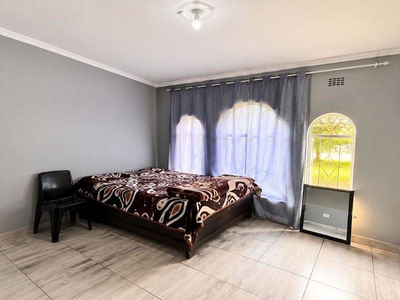 Spacious bedroom featuring neutral grey walls, tiled flooring, built-in cupboards, and distinctive arched windows allowing for natural light.