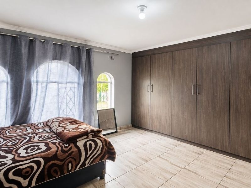 Spacious bedroom featuring extensive built-in cupboards, tiled flooring, and distinctive arched windows, providing ample storage and natural light.