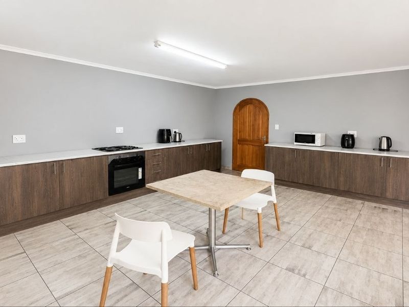 A spacious kitchen featuring modern wood-finish cabinetry, white countertops, a built-in oven, gas hob, and neutral tiled flooring.