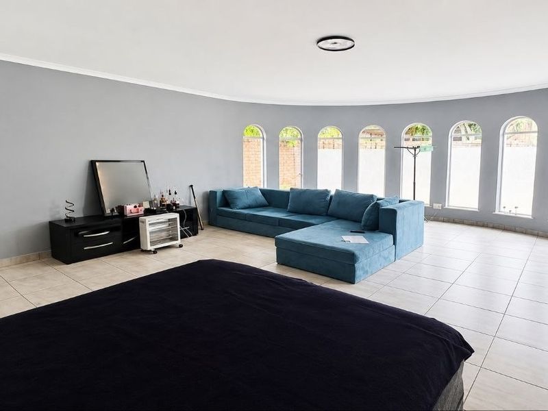 Spacious living room featuring large arched windows, neutral grey walls, and tiled flooring, offering a bright and open layout.