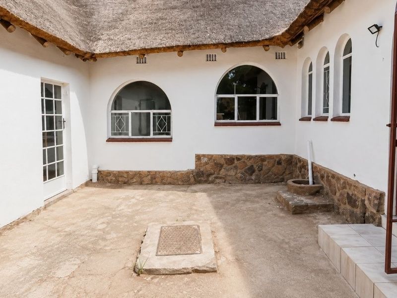 A private rear courtyard featuring a traditional thatch roof, arched windows, and stone-clad base, offering a blank canvas for outdoor living space development.