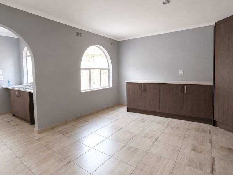 An open-plan living area featuring neutral grey walls, tiled flooring, built-in dark wood cabinetry, and an elegant arched window.