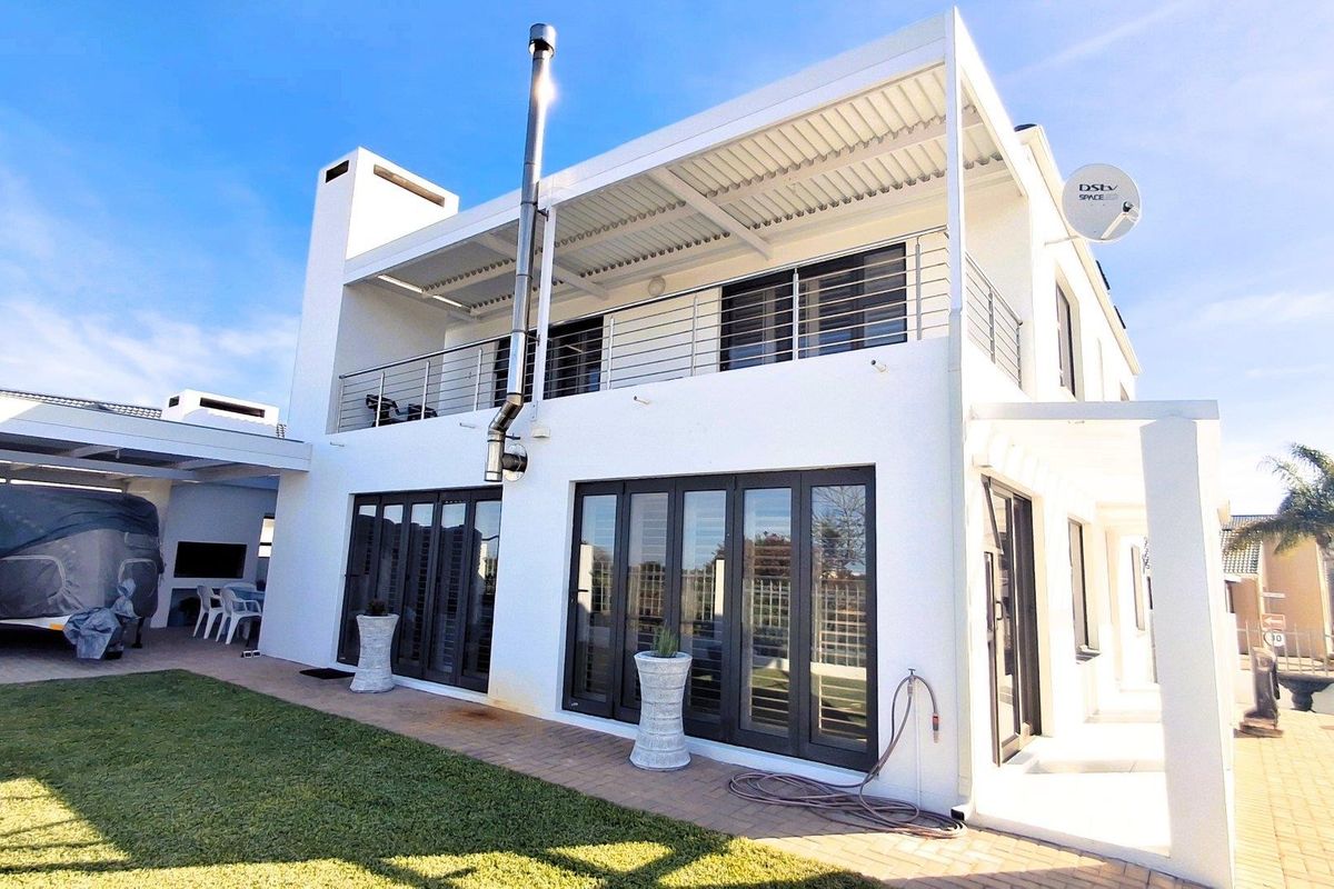 Rear view of a modern two-story house featuring a covered patio, upper balcony with stainless steel balustrades, and large folding glass doors.