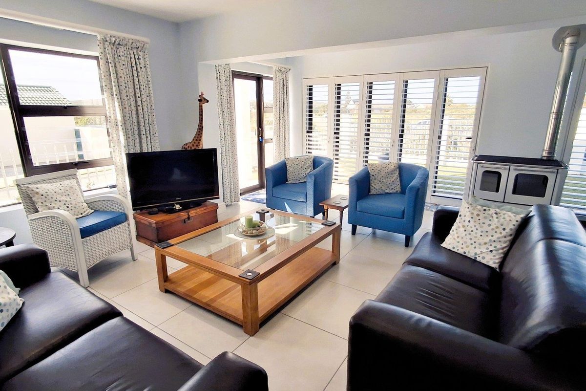 Spacious living room featuring large tiled flooring, a built-in wood-burning fireplace, and plantation shutters providing access to the outdoor area.