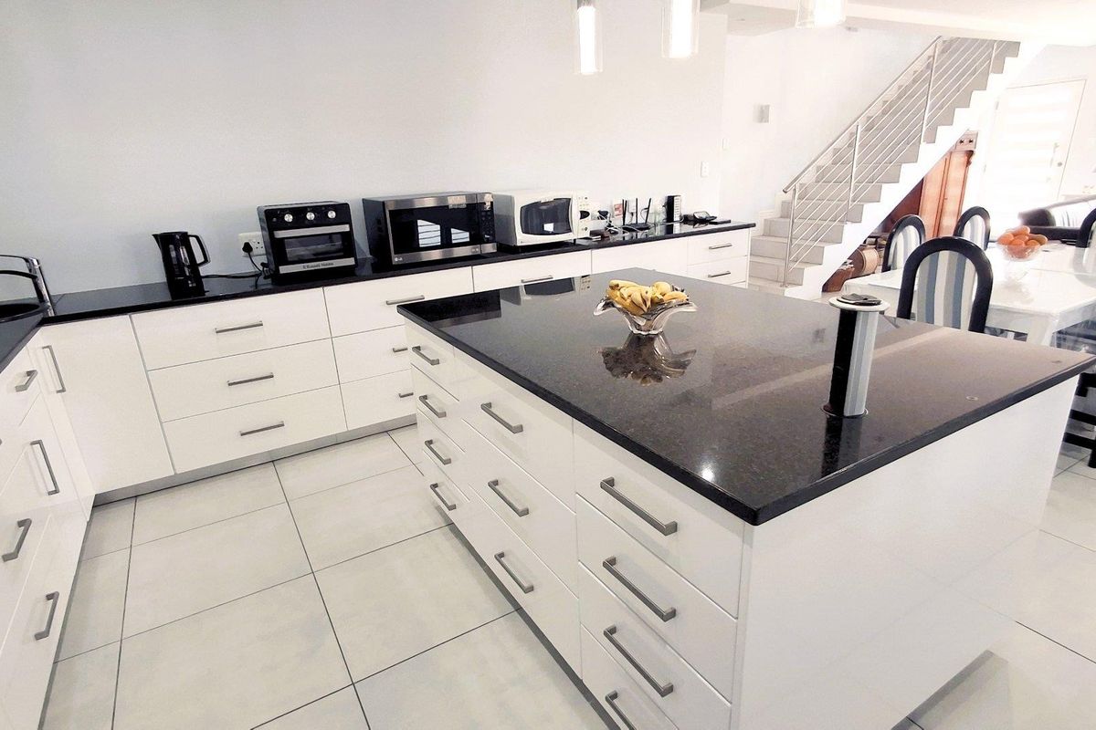 Modern kitchen featuring white cabinetry, black granite countertops, a central island with a pop-up power outlet, and tiled flooring, adjacent to an open staircase.