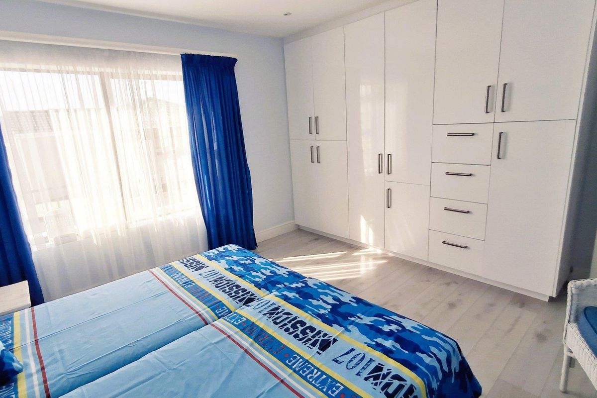 A well-maintained bedroom featuring extensive white built-in cupboards, light-toned laminate flooring, and natural light through a large window.