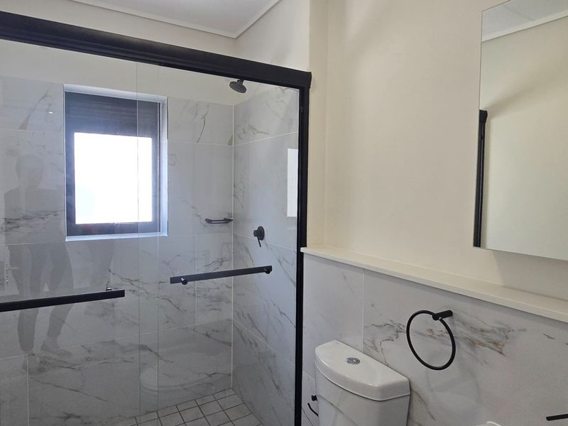 Modern bathroom featuring a walk-in shower with black-framed glass enclosure, marble-look wall tiles, and contemporary fixtures.