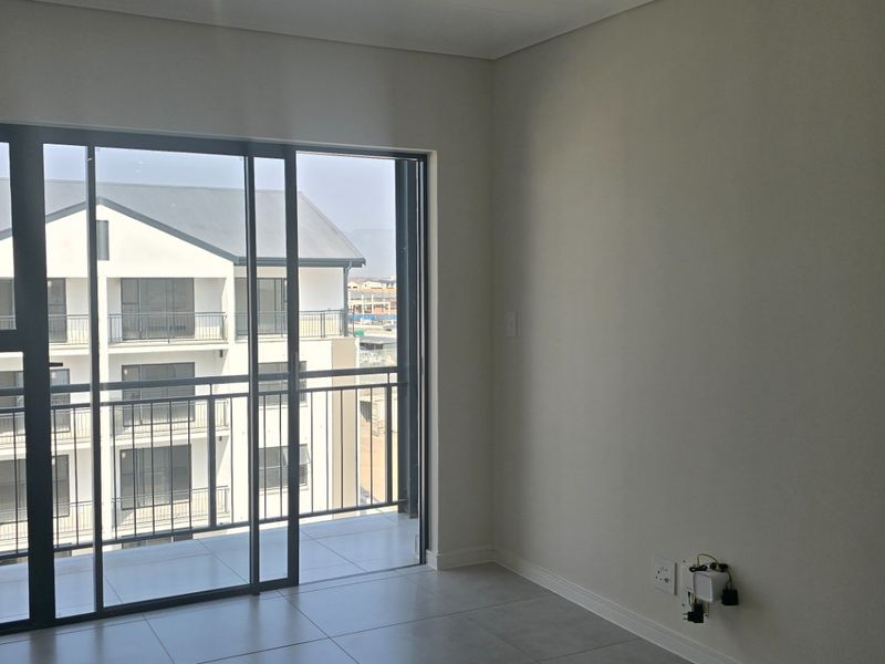 A bright, empty bedroom featuring neutral tiled flooring and a large sliding glass door that opens onto a private balcony.