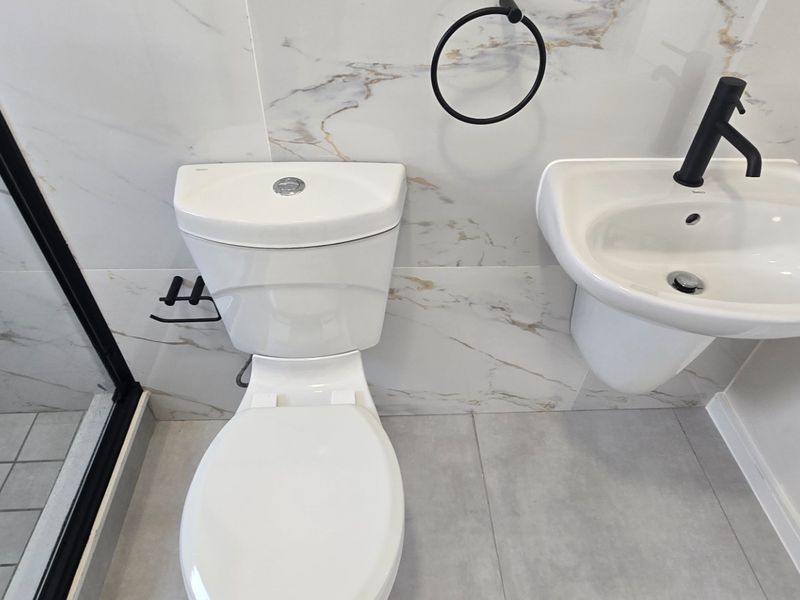 Modern bathroom featuring marble-effect wall tiles, a wall-mounted basin with a black mixer tap, a toilet, and a glass-enclosed shower.