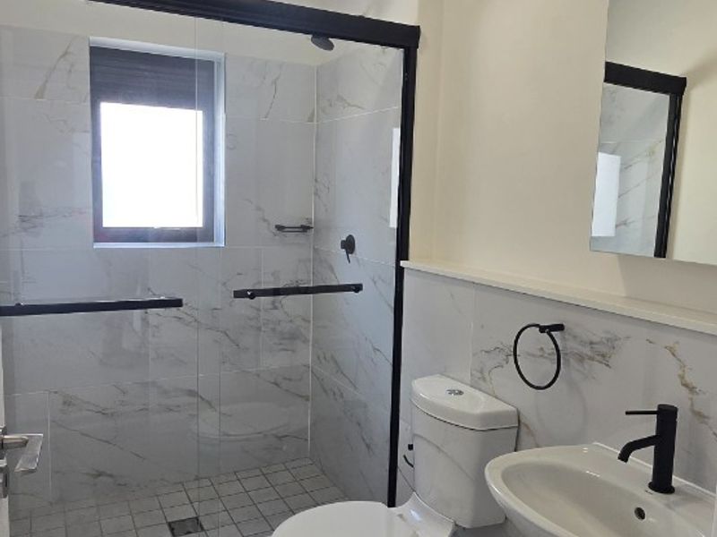 Modern bathroom featuring a walk-in shower with black-framed glass, marble-look wall tiles, a pedestal basin with black fixtures, and a clean, contemporary finish.