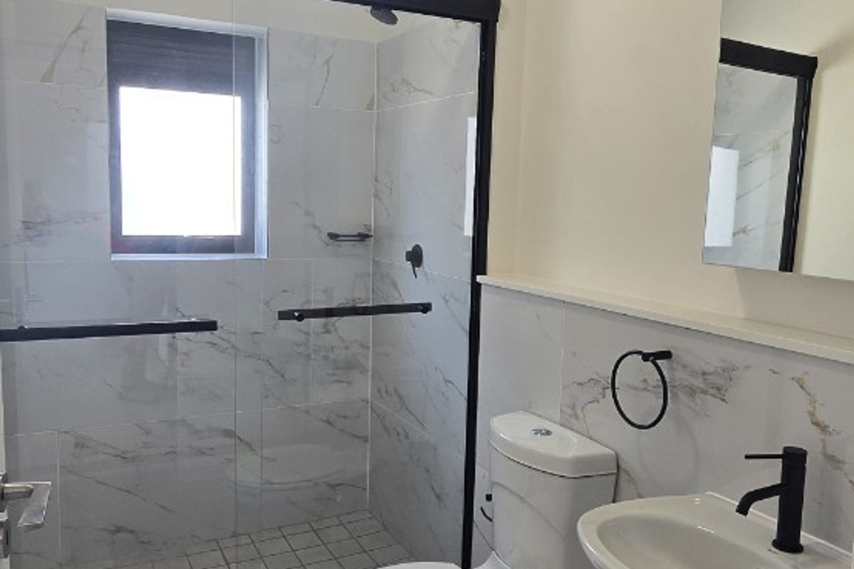 Modern bathroom featuring a walk-in shower with black-framed glass, marble-look wall tiles, a pedestal basin with black fixtures, and a clean, contemporary finish.