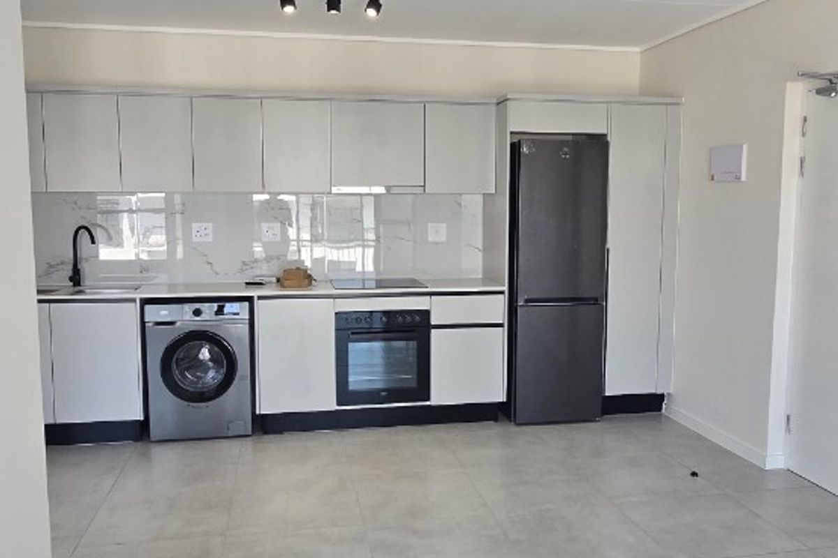 Modern open-plan kitchen featuring sleek white cabinetry, integrated appliances, tiled flooring, and contemporary spotlighting in a clean, minimalist space.