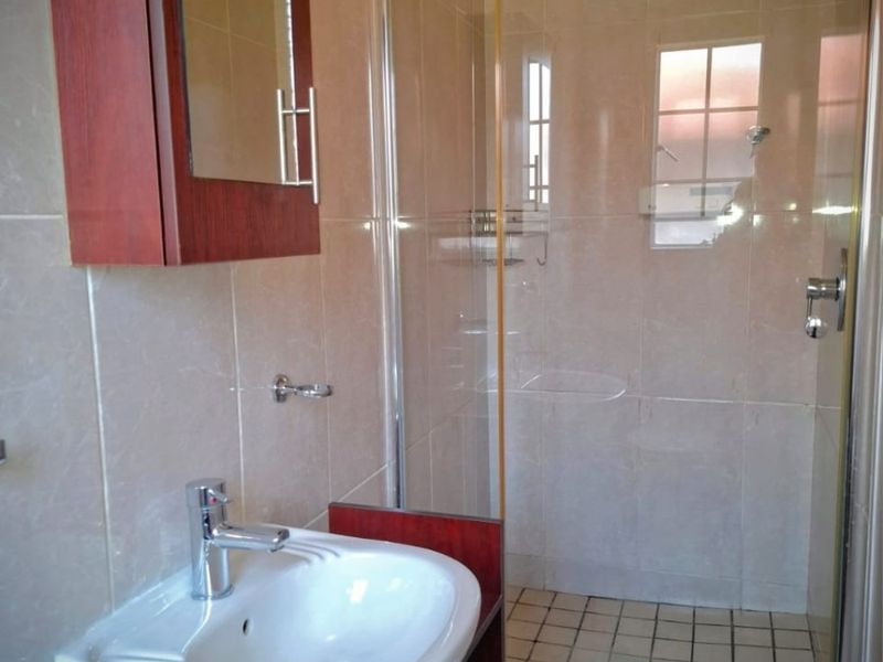 A clean bathroom featuring a vanity cabinet with a ceramic basin, a wall-mounted medicine cabinet, and a glass-enclosed shower with tiled finishes.