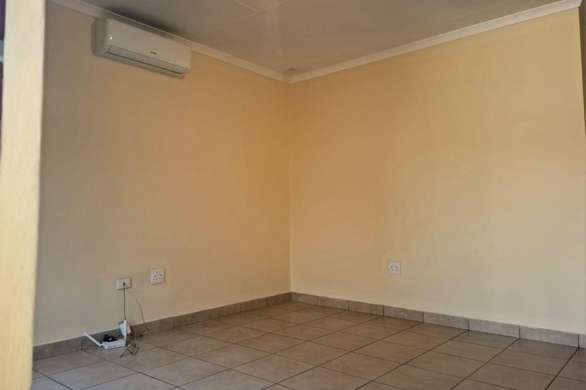 An empty living room featuring tiled flooring, neutral walls, and a wall-mounted split-system air conditioning unit.